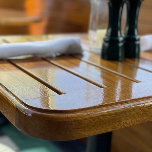 Close-up view of a polished wooden dining table featuring sleek grooves, with folded napkins and a salt and pepper set placed on top.