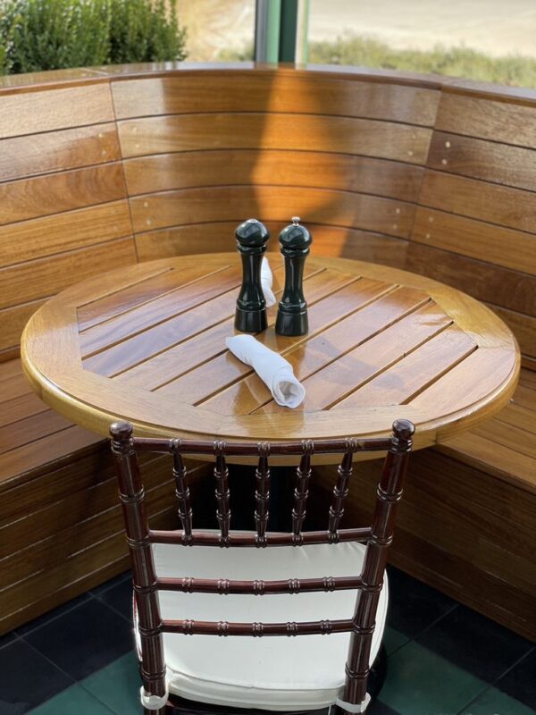 A round wooden table with salt and pepper shakers, set in front of a curved wooden bench and a single wooden chair.