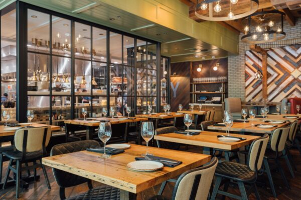 South Loft custom wooden tables and upholstered chairs in a modern restaurant with an open kitchen.