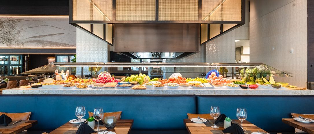 A vibrant restaurant buffet setup featuring colorful fresh fruits and vegetables, designed by South Loft with a sleek and modern layout, including leather seating and wooden tables.