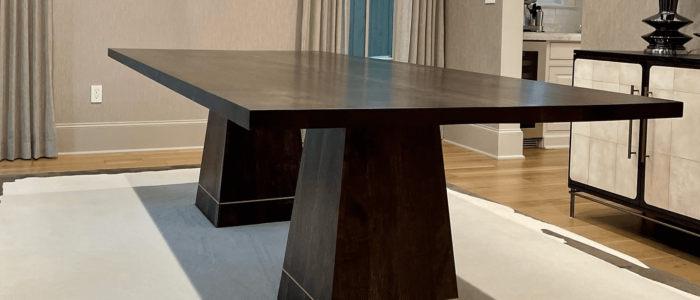 South Loft custom rectangular dining table with dark wood finish and tapered pedestal legs, placed in an elegant dining room with beige walls and light wood floors.