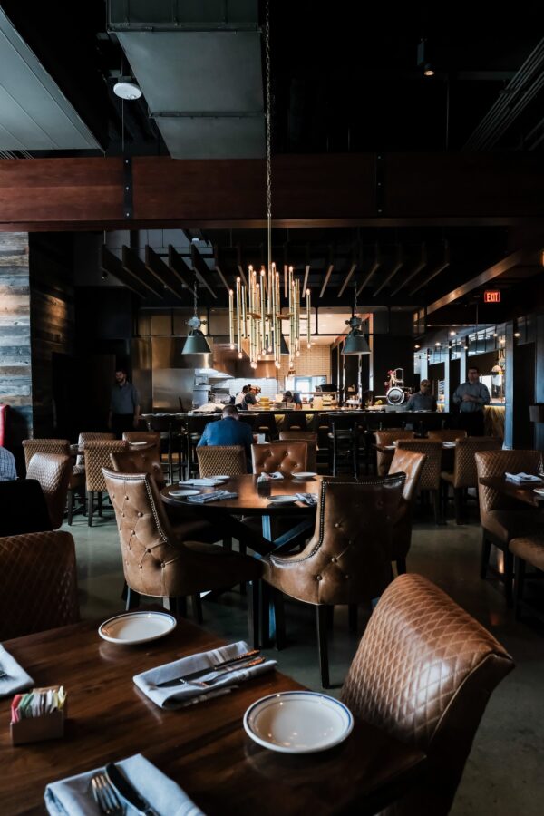 South Loft walnut dining tables with quilted leather chairs and modern chandelier in upscale restaurant.