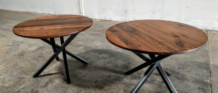 Two round South Loft custom side tables with dark wood tops and black metal crisscross legs.